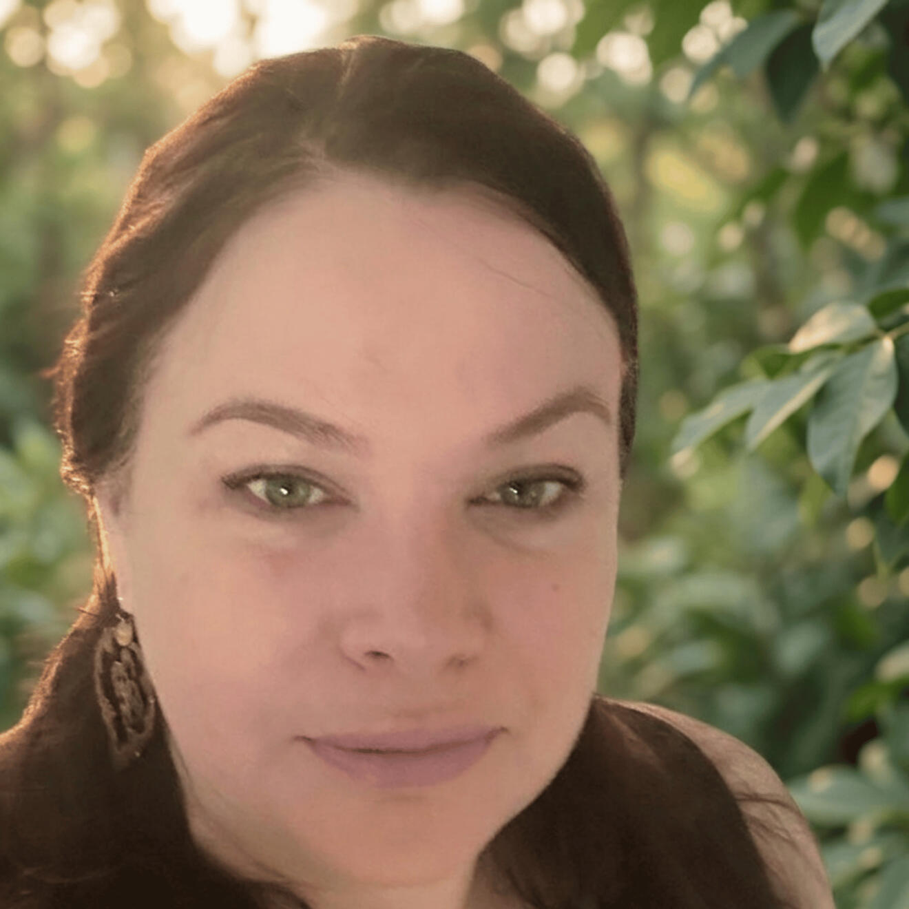 Caroline Jane, Emotion Code and Body Code practitioner, outdoors under green foliage